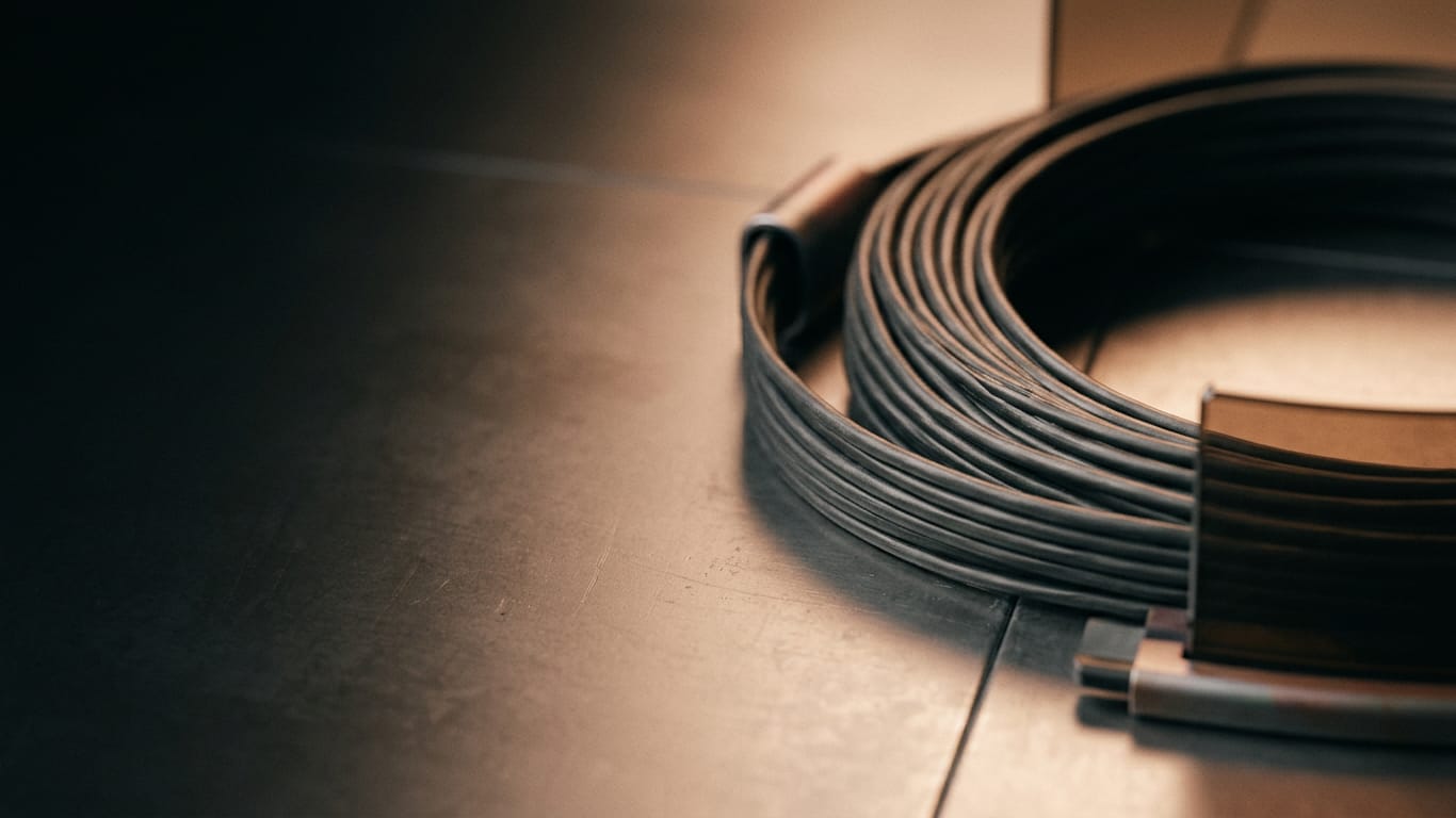 Illustration for this article: serious cyber threat from AI agents within months. A coil of unbranded ribbon cable unspooling across a matte floor into darkness.