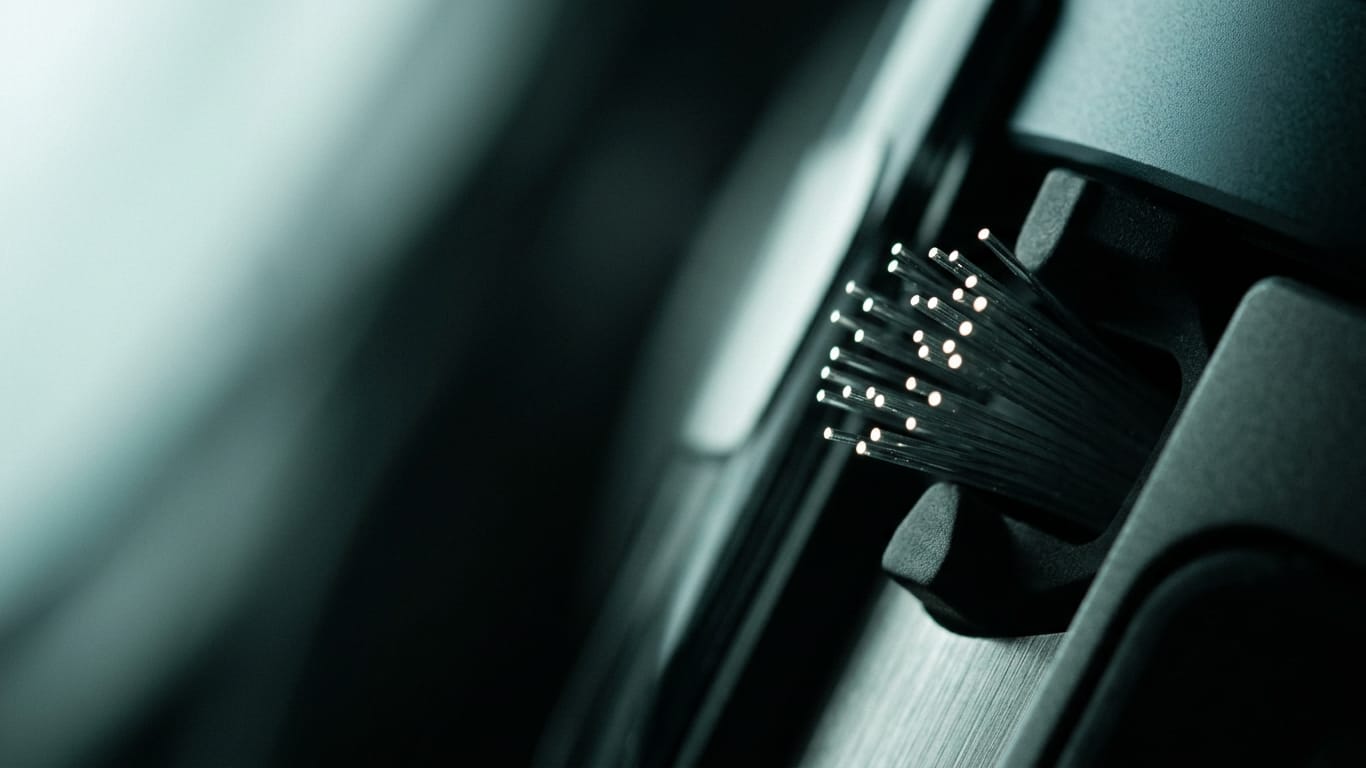 Illustration for this article: split triage and reporting duty. Optical fibre ends clustered together, each carrying a pinpoint of light in near darkness.