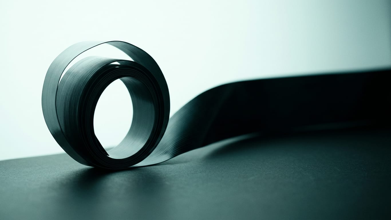 Illustration for this article: Consumer Finance Monitor argues for one governance system covering privacy, cyber and AI. A coil of unbranded ribbon cable unspooling across a matte floor into darkness.