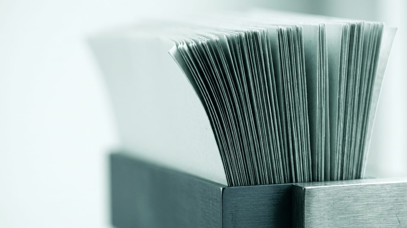 Illustration for this article: DHS excludes DeepSeek and third-party products. The cut edges of a thick stack of blank paper, fanned slightly, raking light along the fibres.
