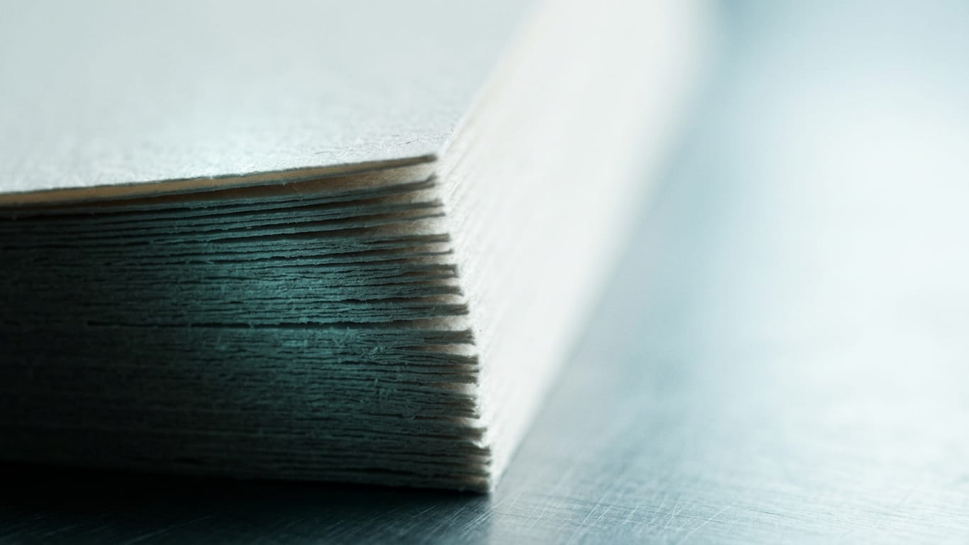 Illustration for this article: Document Redlining Software for Regulated Teams. The cut edges of a thick stack of blank paper, fanned slightly, raking light along the fibres.