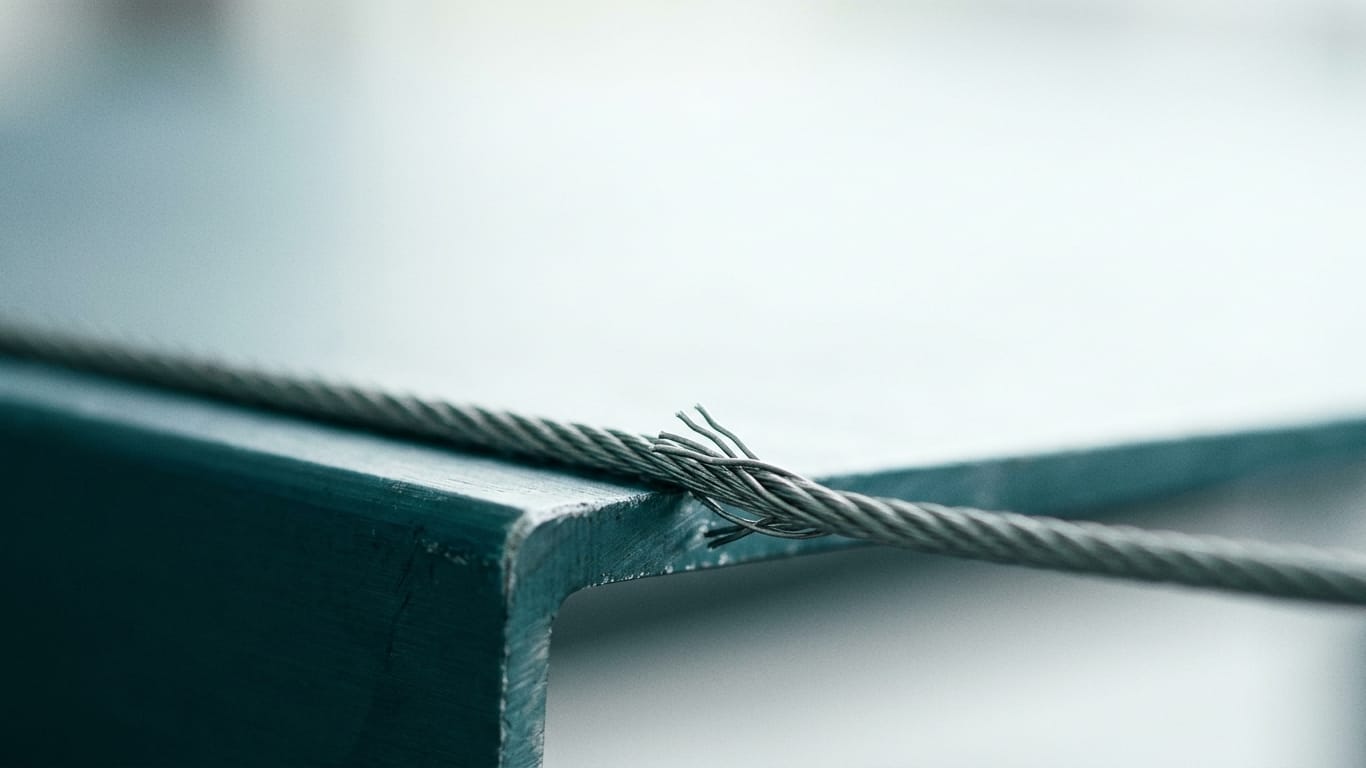 Illustration for this article: EU transparency rules mandate AI output validation from August 2026. A steel cable under visible tension, strands separating where it passes over an edge.