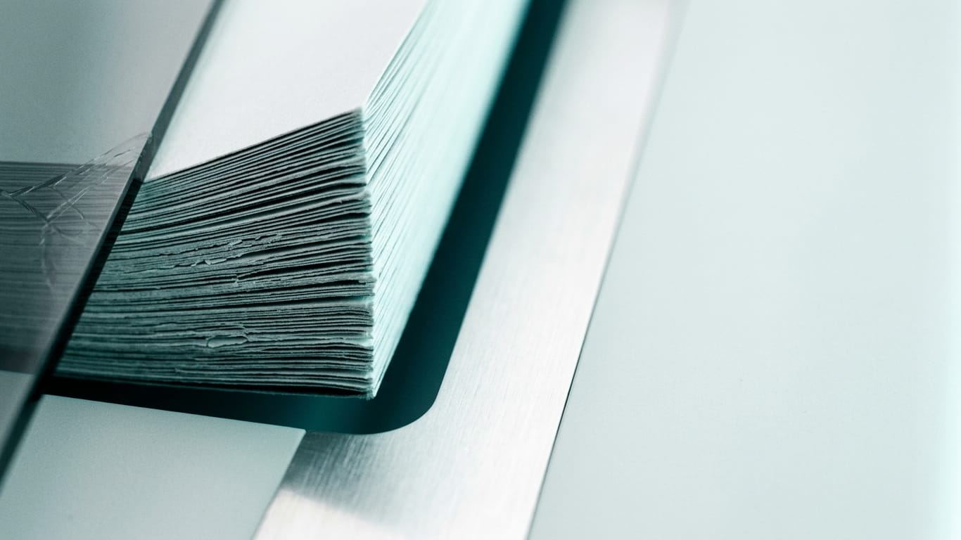 Illustration for this article: Explainability is not an audit trail. The cut edges of a thick stack of blank paper, fanned slightly, raking light along the fibres.