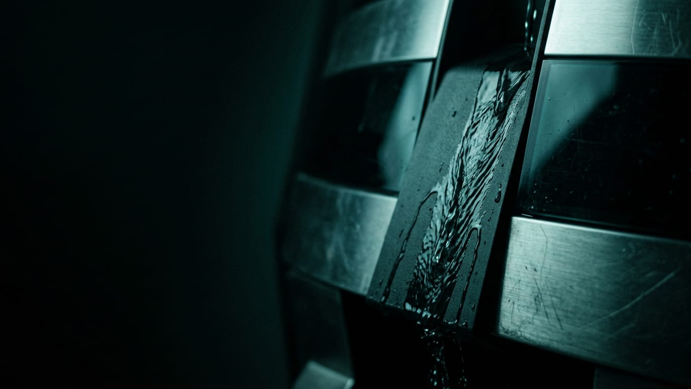 Illustration for this article: Frontier training under a safety case. Water sheeting down a matte dark surface, breaking around an unseen obstruction.
