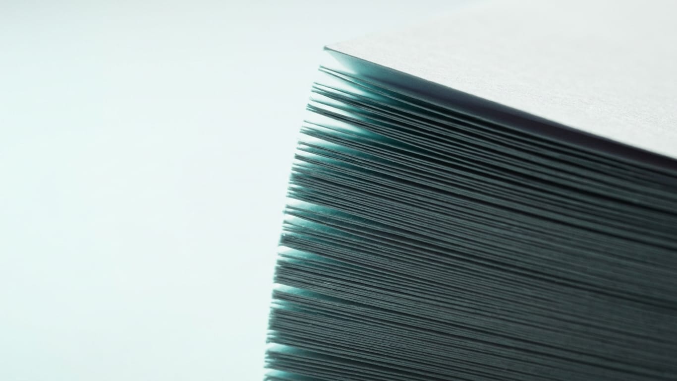 Illustration for this article: New EU Transparency Rules Make AI Output Validation Demonstrable. The cut edges of a thick stack of blank paper, fanned slightly, raking light along the fibres.