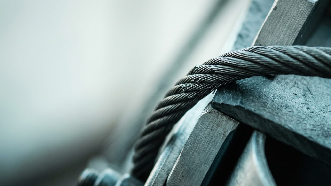 Illustration for this article: Oberlandesgericht Hamm held a company responsible. A steel cable under visible tension, strands separating where it passes over an edge.