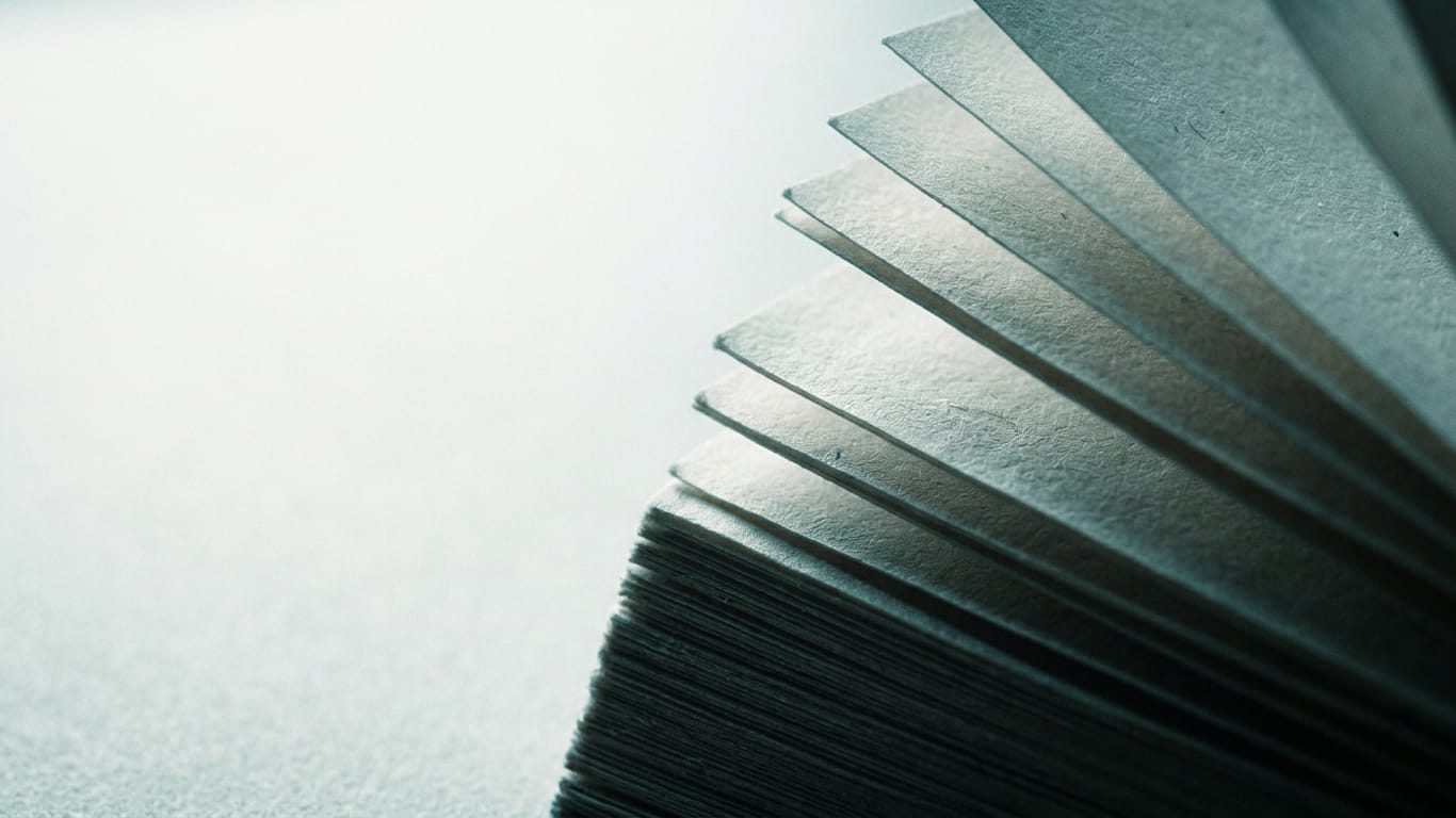 Illustration for this article: Open-weight AI models vulnerable to jailbreaks. The cut edges of a thick stack of blank paper, fanned slightly, raking light along the fibres.