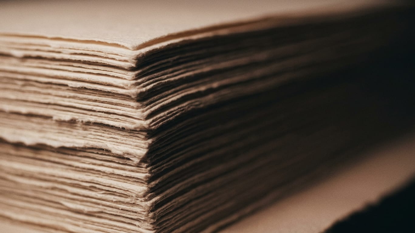 Illustration for this article: Secure private LLM inference in layers. The cut edges of a thick stack of blank paper, fanned slightly, raking light along the fibres.