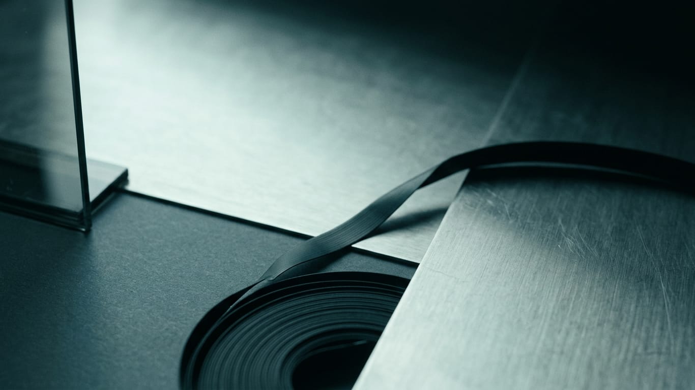 Illustration for this article: What an AI-driven claimant like Morgan & Morgan means for your defence and evidence strategy. A coil of unbranded ribbon cable unspooling across a matte floor into darkness.