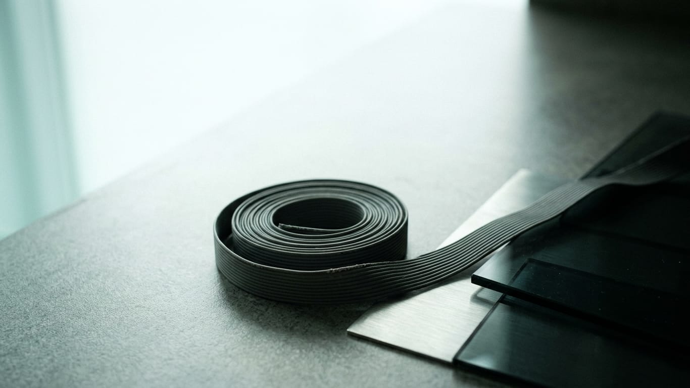 Illustration for this article: Why a wrong AI answer becomes traceable. A coil of unbranded ribbon cable unspooling across a matte floor into darkness.